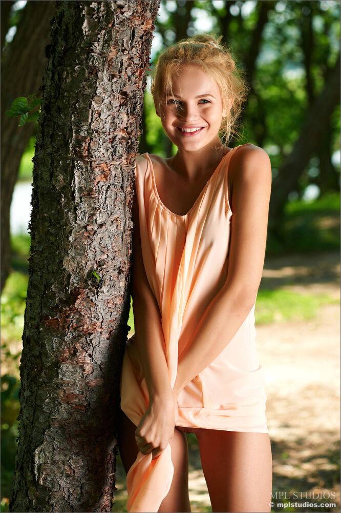 Smiley cute teen in short dress disrobes to pose nude under a tree - #4