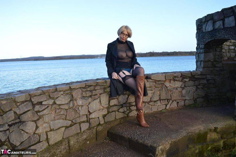 Mature blonde Barby Slut exposes her tits and twat in leather coat by a river - #15