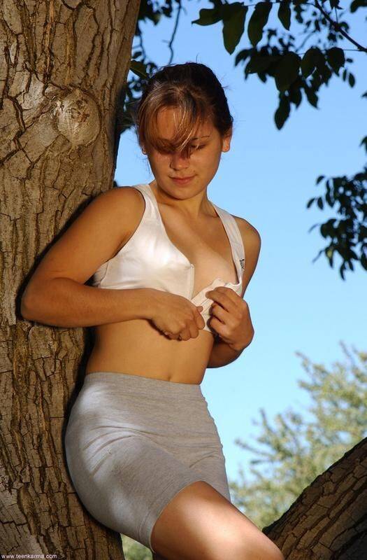 Petite teen Karma strips off her clothes to pose nude up in a tree - #15