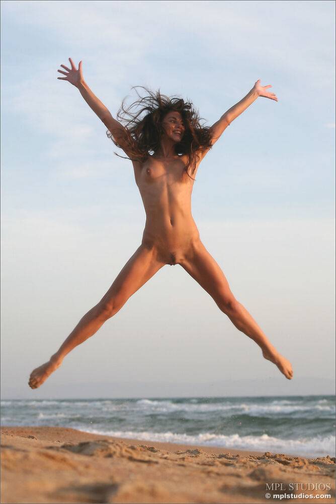 Pretty girl leaps into the air while completely naked on a beach - #3