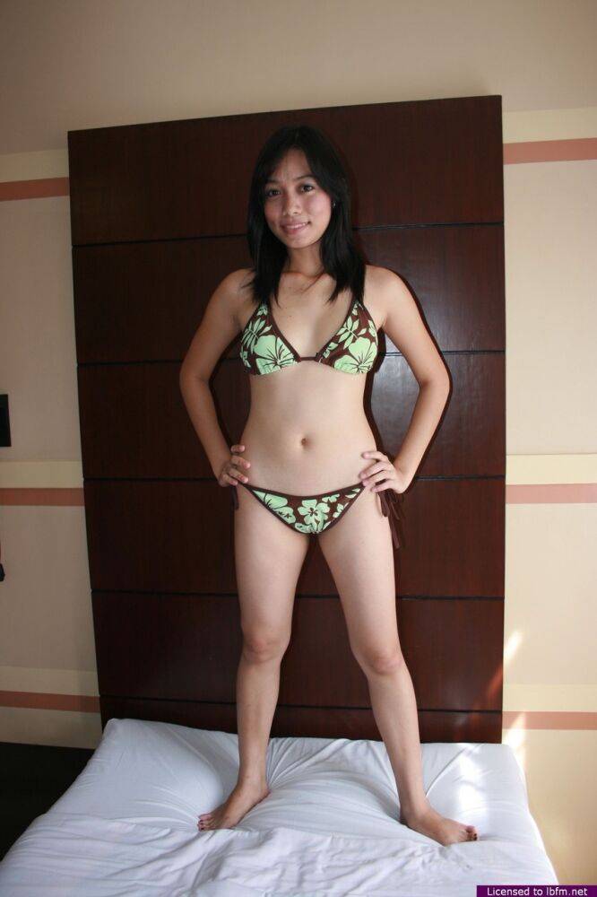Young Asian girl Janelyn stands naked after removing her bikini on a bed | Photo: 2325529