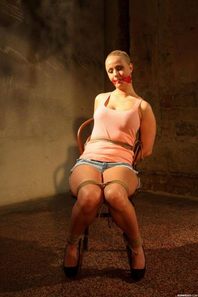 Blonde female in denim shorts is gagged and tied to a chair in an empty room - #8