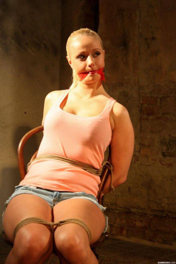 Blonde female in denim shorts is gagged and tied to a chair in an empty room - #6