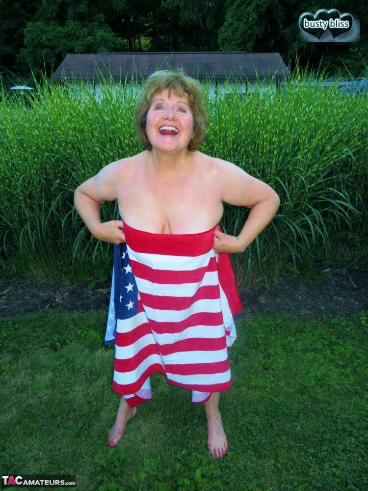 Older plumper Busty Bliss holds an American flag while totally naked in a yard - #4