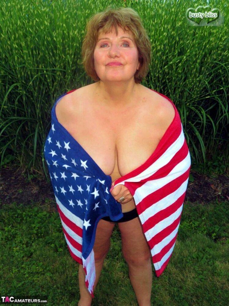 Older plumper Busty Bliss holds an American flag while totally naked in a yard - #6