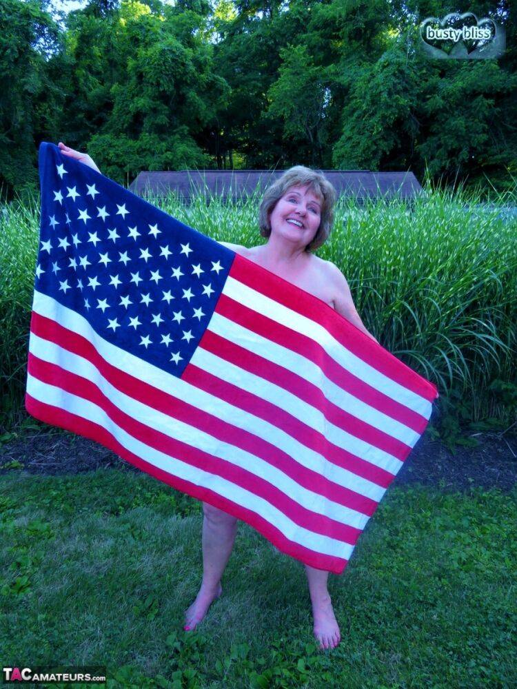 Older plumper Busty Bliss holds an American flag while totally naked in a yard - #10