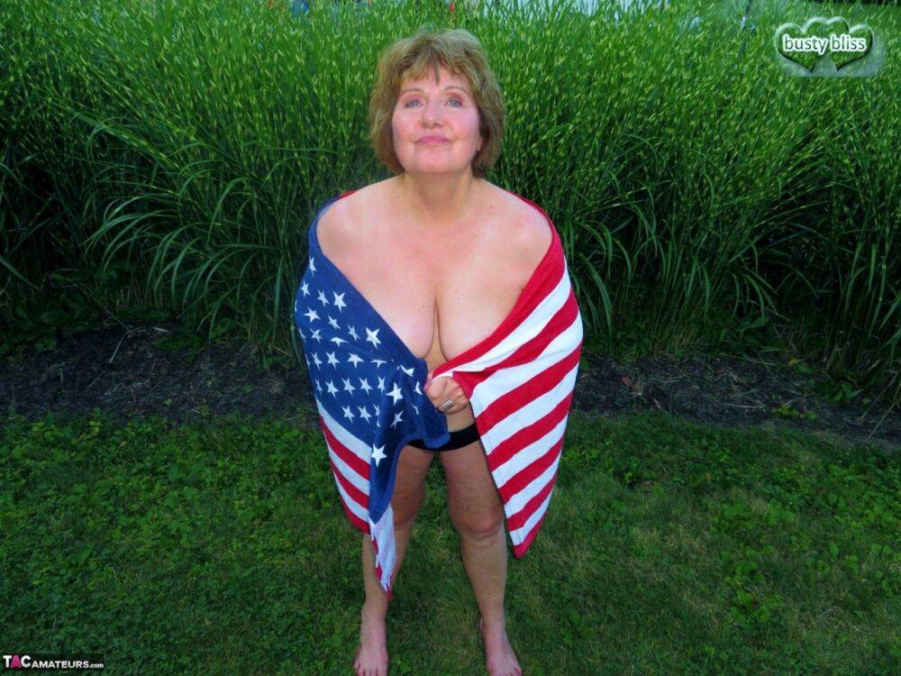 Older plumper Busty Bliss holds an American flag while totally naked in a yard - #7