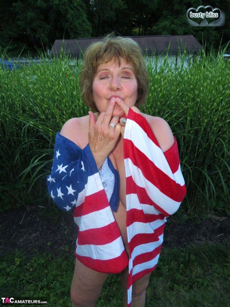 Older plumper Busty Bliss holds an American flag while totally naked in a yard - #8