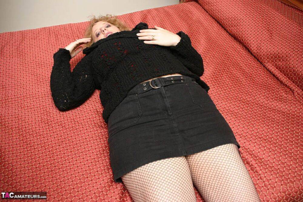 Older woman Curvy Claire undoes her brassiere on a bed in a skirt and boots - #3