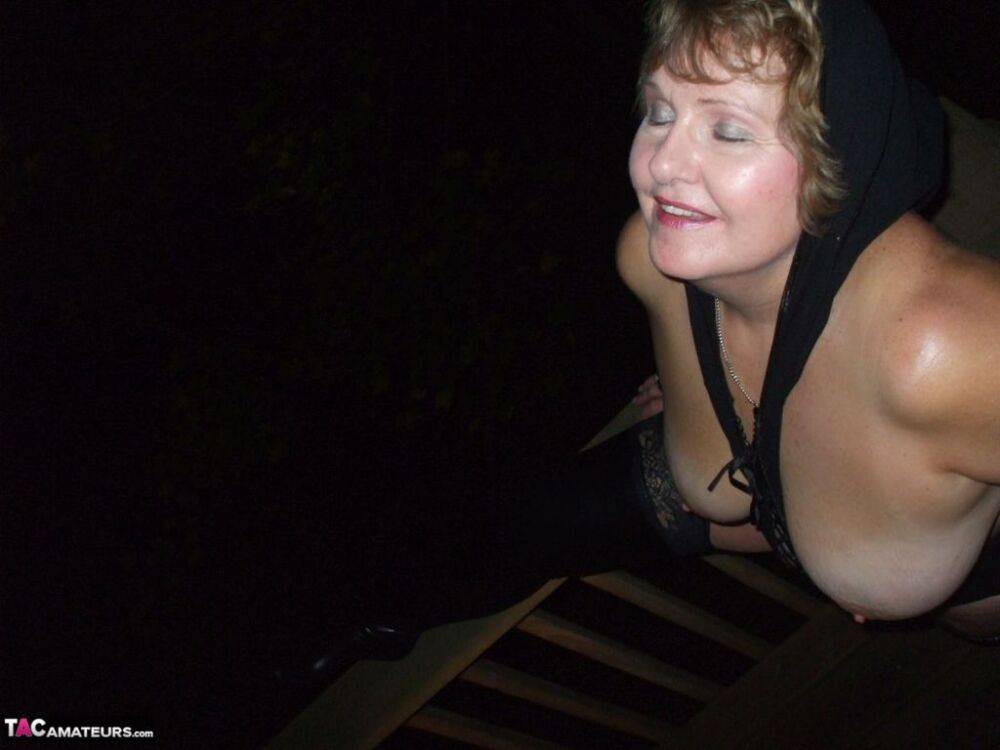 Older woman Busty Bliss displays her big naturals at night while on a deck - #10