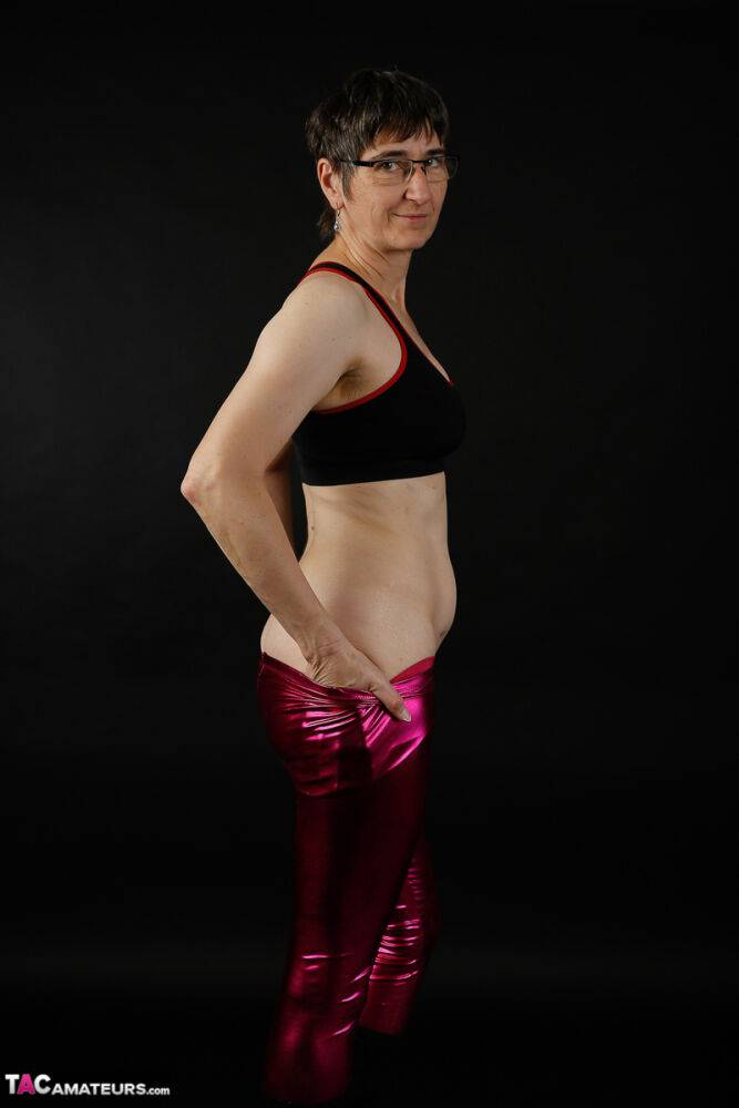 Mature woman models a sports bra in shiny pants and black boots - #3
