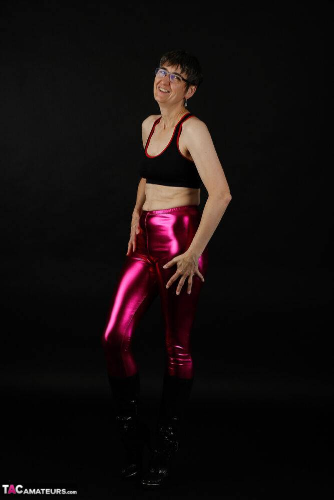 Mature woman models a sports bra in shiny pants and black boots - #10