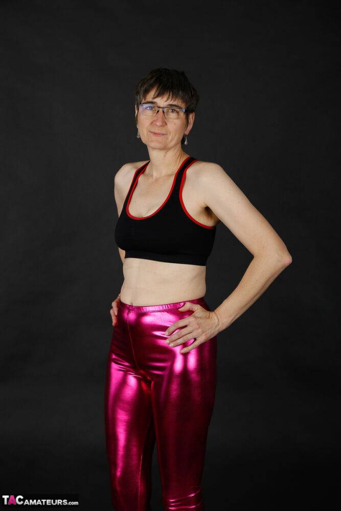 Mature woman models a sports bra in shiny pants and black boots - #6