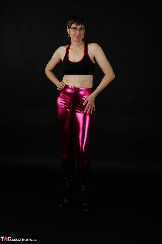 Mature woman models a sports bra in shiny pants and black boots - #2