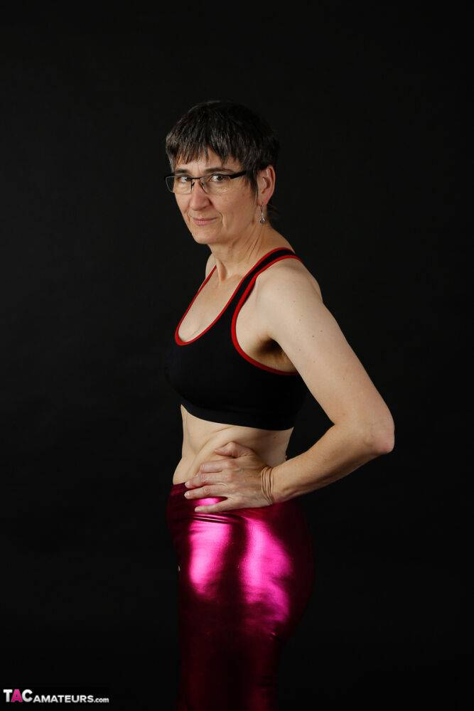 Mature woman models a sports bra in shiny pants and black boots - #5