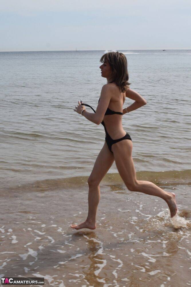 Slender female models a bathing suit while at a deserted beach - #16