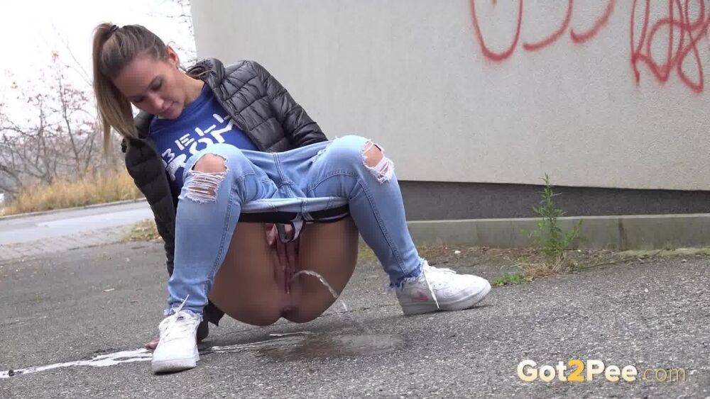 Czechoslovakian female Naomi Bennet takes a pee on pavement beside a building - #13