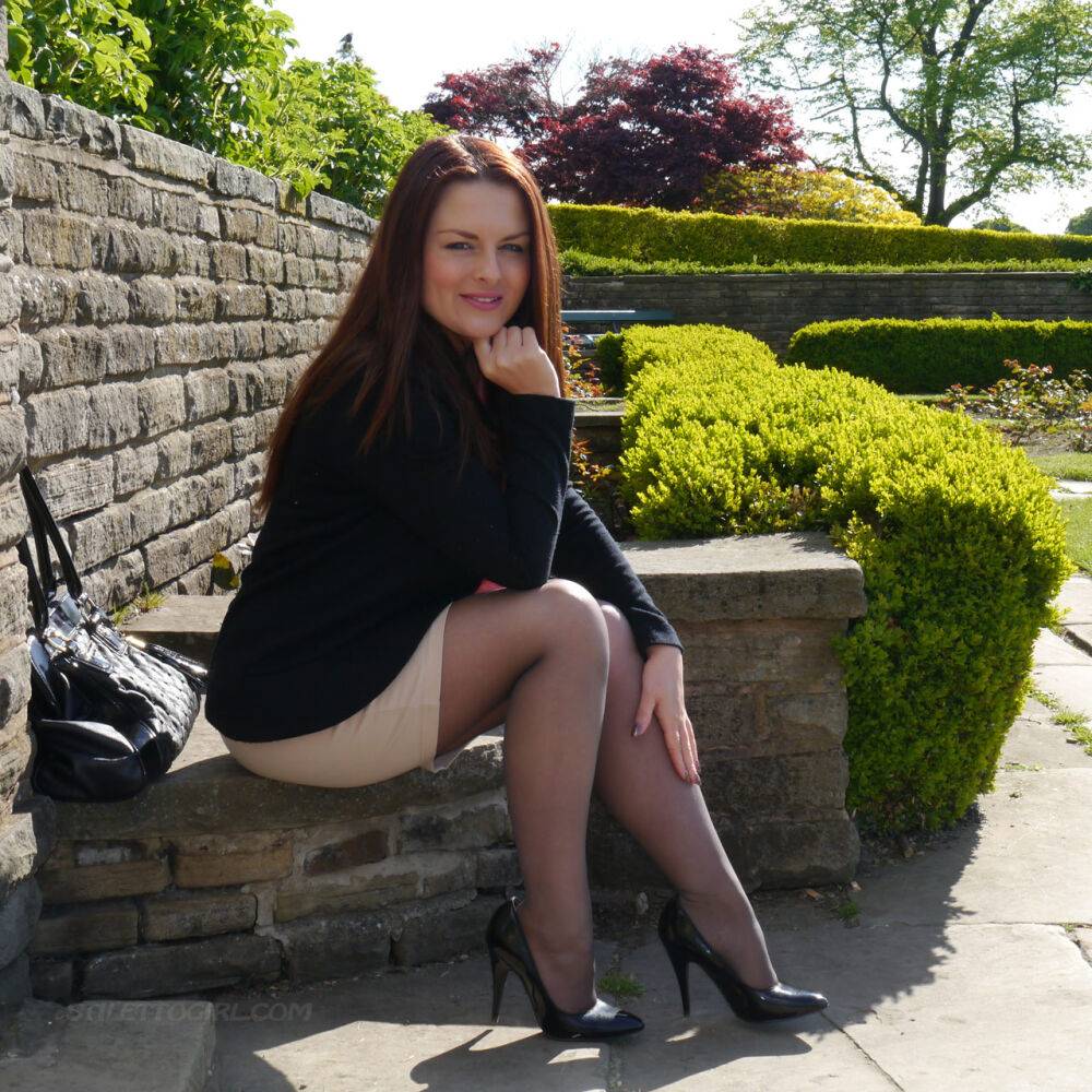 Clothed redhead Sara shows off her black heels on a sidewalk in hosiery - #1