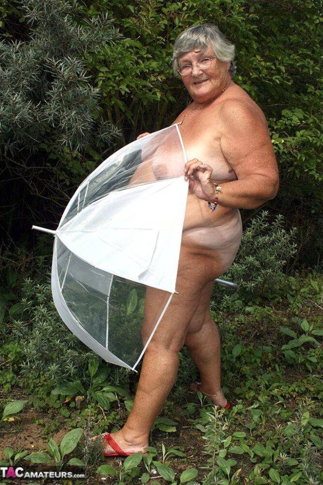 Obese oma Grandma Libby holds an umbrella while posing naked by fir trees - #6