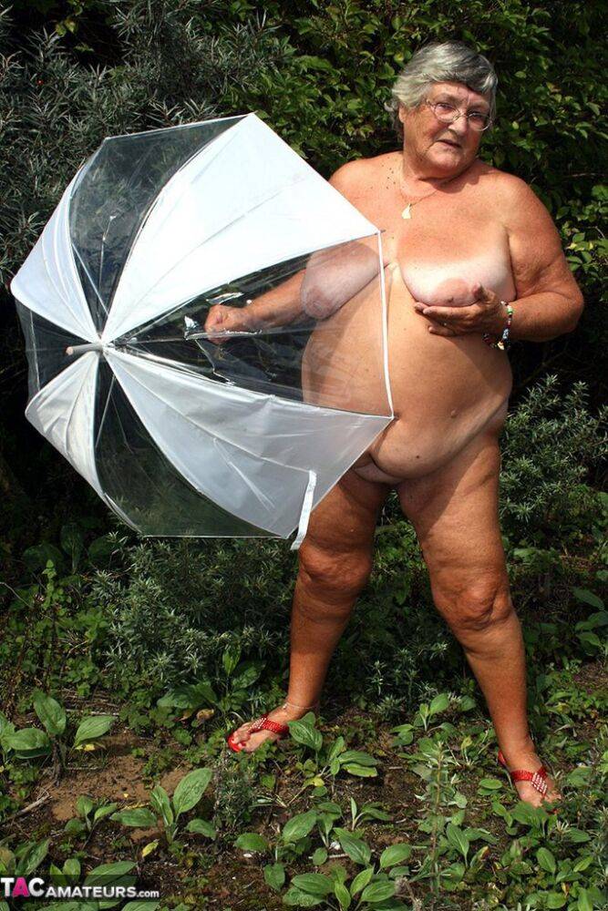 Obese oma Grandma Libby holds an umbrella while posing naked by fir trees - #16