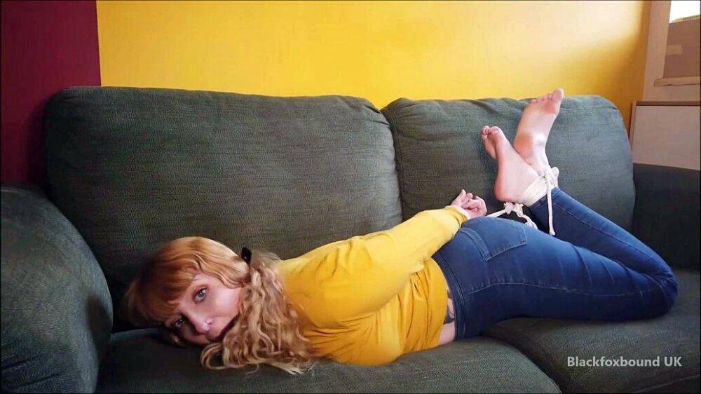 Barefoot white girl is hogtied on a sofa while ball gagged in her clothing - #12