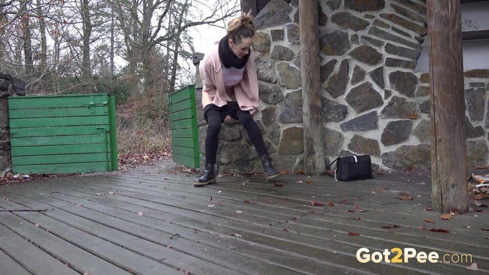 White girl Cynthia Vellons takes a piss on a deck behind a stone structure - #1