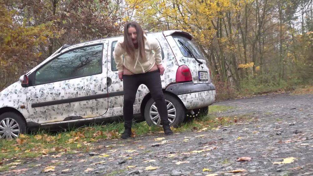 White girl Nicolette Noir takes a piss beside a parked car in a wooded setting - #14