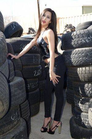 Latina amateur Bella Quinn covers her naked tits with hands amid tire stacks on pornstar6.com