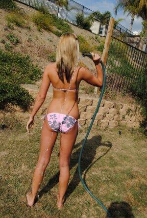 Young blonde girl in a bikini soaks herself with a garden hose on pornstar6.com