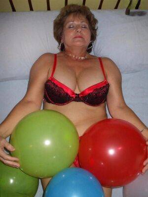 Mature woman Busty Bliss goes topless on her bed while playing with balloons on pornstar6.com