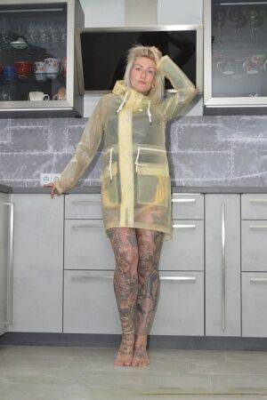 Tattooed blonde Miss Francine models barefoot in a raincoat over rubber wear on pornstar6.com