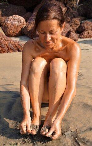 Naked older woman Diana Ananta covers her feet in beach sand at low tide on pornstar6.com