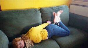 Barefoot white girl is hogtied on a sofa while ball gagged in her clothing on pornstar6.com